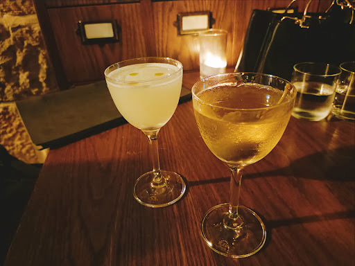 Two cocktails in coupe glasses by a candlelit table
